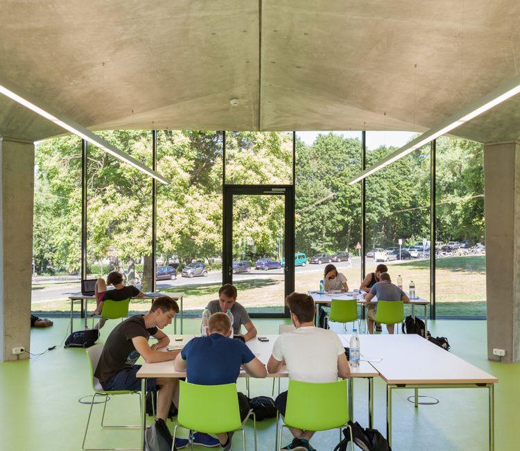 Studierende beim Arbeiten im lichtdurchfluteten Lernraum mit grünen Stühlen.