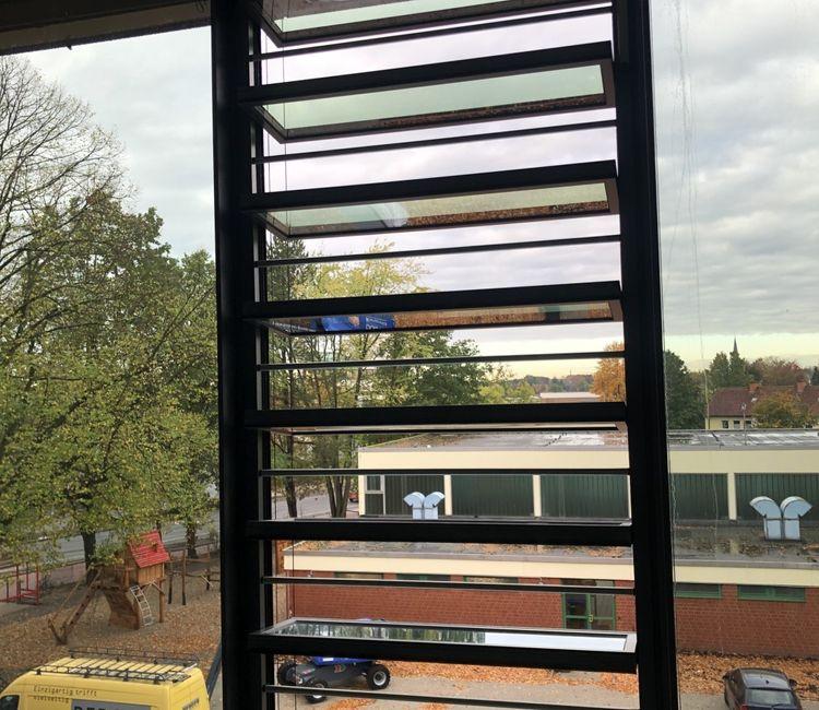 Nahaufnahme eines Fensterflügels mit Lamellenlüftung und Blick nach draußen