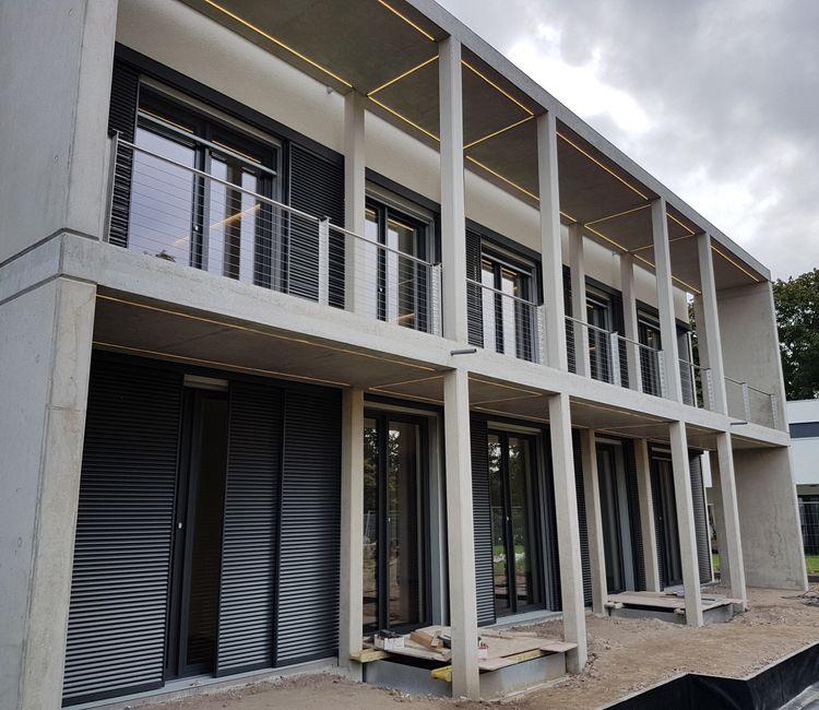 Moderne Doppelhaushälfte mit klarer Betonfassade und integrierter LED-Beleuchtung.
