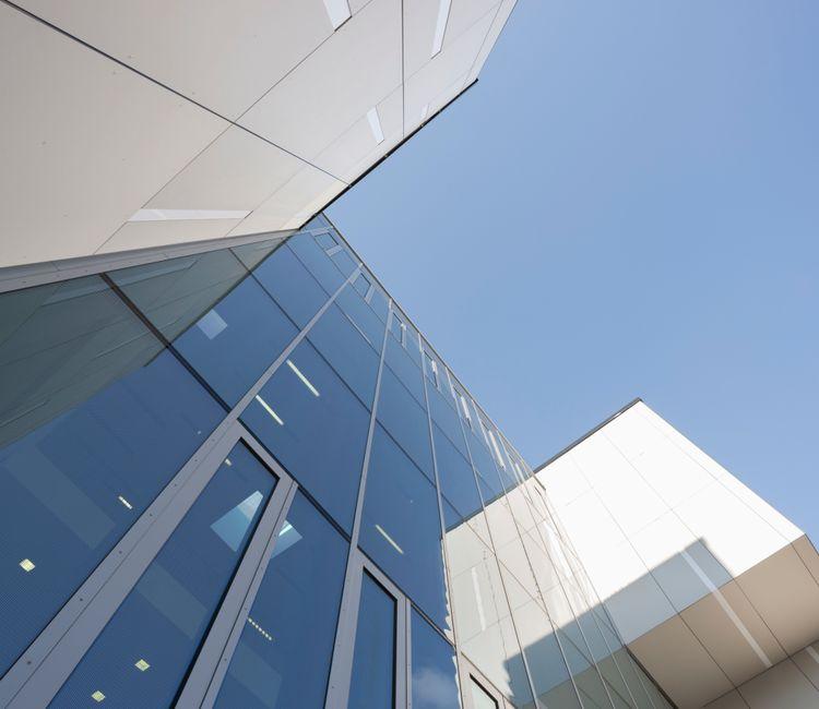 Detailansicht der Glasfassade mit reflektierendem Himmel und Fensterelementen.