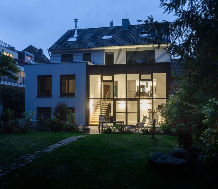 Gesamtansicht des umgebauten Hauses mit angebautem Wintergarten und stimmungsvollem Garten im Vordergrund.