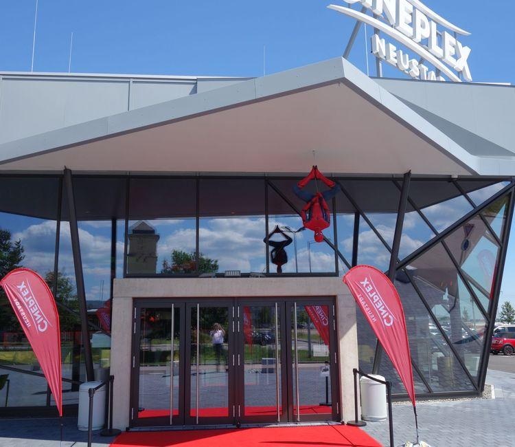Frontansicht des Eingangsbereichs des Cineplex Neustadt mit Spiderman-Figur und rotem Teppich.