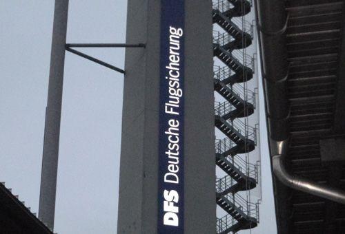 Beleuchtetes DFS-Logo an einem Flugsicherungsturm in der Dämmerung.