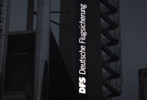DFS-Schriftzug bei Nacht, vertikal am Turm angebracht mit externer Treppe im Hintergrund.