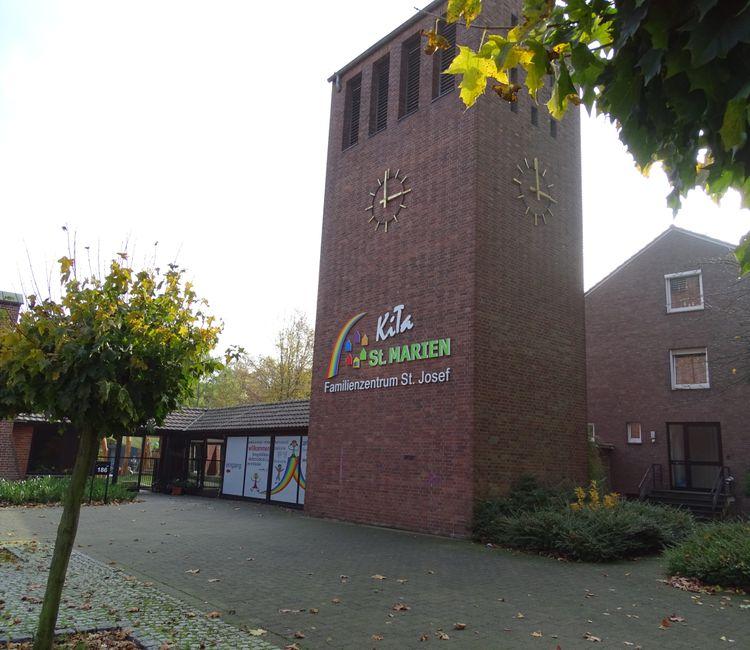 Seitlicher Blick auf den Glockenturm mit buntem KiTa-Logo und angrenzendem Verbindungsgang.