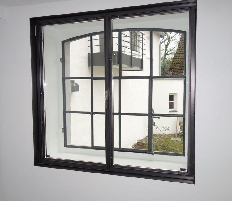 Innenfenster mit schwarzem Sprossenrahmen und Blick auf den Innenhof mit weißer Fassade.