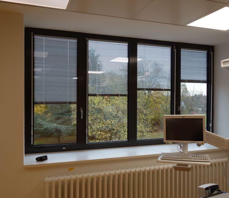 Blick aus einem Klinikraum auf moderne Fenster mit innenliegendem Sonnenschutz.