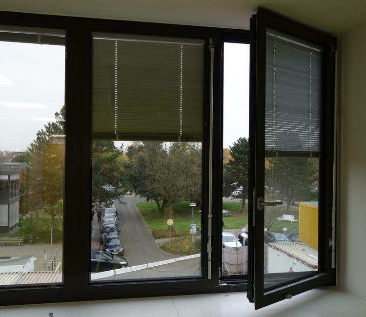 Fenster mit geöffnetem Flügel und Blick auf den Klinikparkplatz.