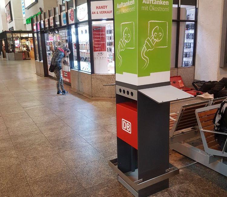 Ladesäule der Deutschen Bahn in Bahnhofshalle vor einem Handy-Shop