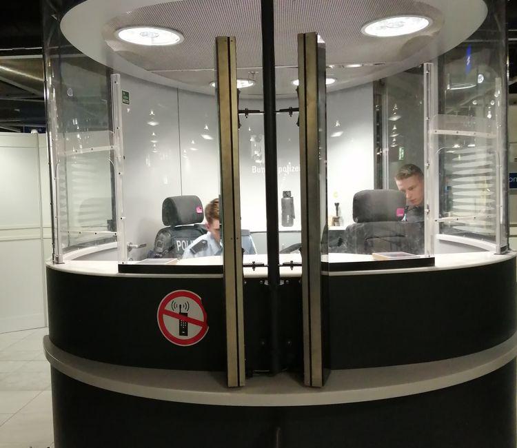 Zwei Beamte sitzen in einer runden Passkontrollkabine der Bundespolizei.