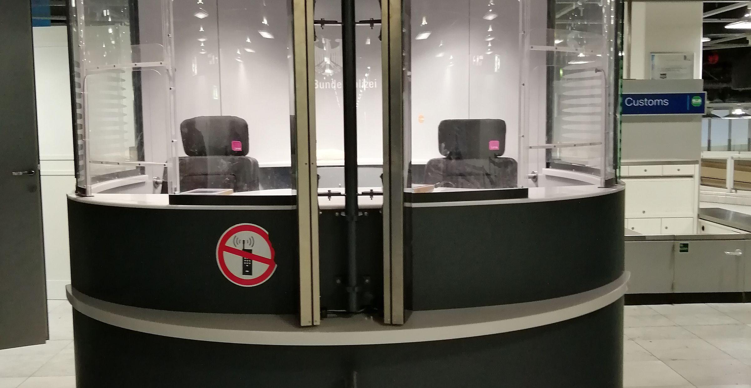 Moderne Passkontrollstelle mit zwei leeren Stühlen hinter Sicherheitsglas.