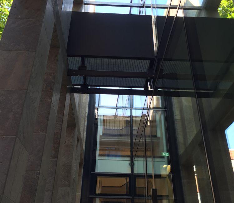Detailansicht eines Glasbalkons mit sichtbaren Stahlträgern und Glasverbindungen.