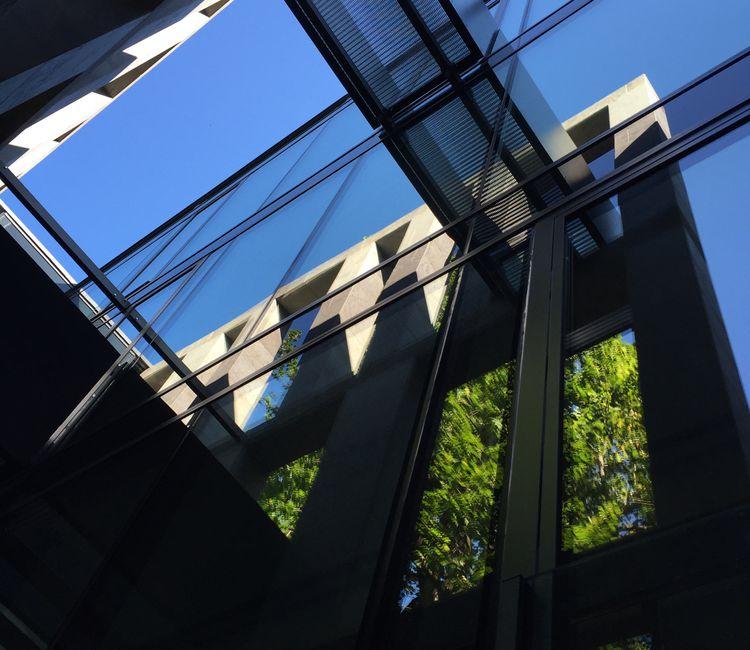 Blick nach oben auf zwei durch Glas verbundene Gebäudeteile mit Brückenelement.