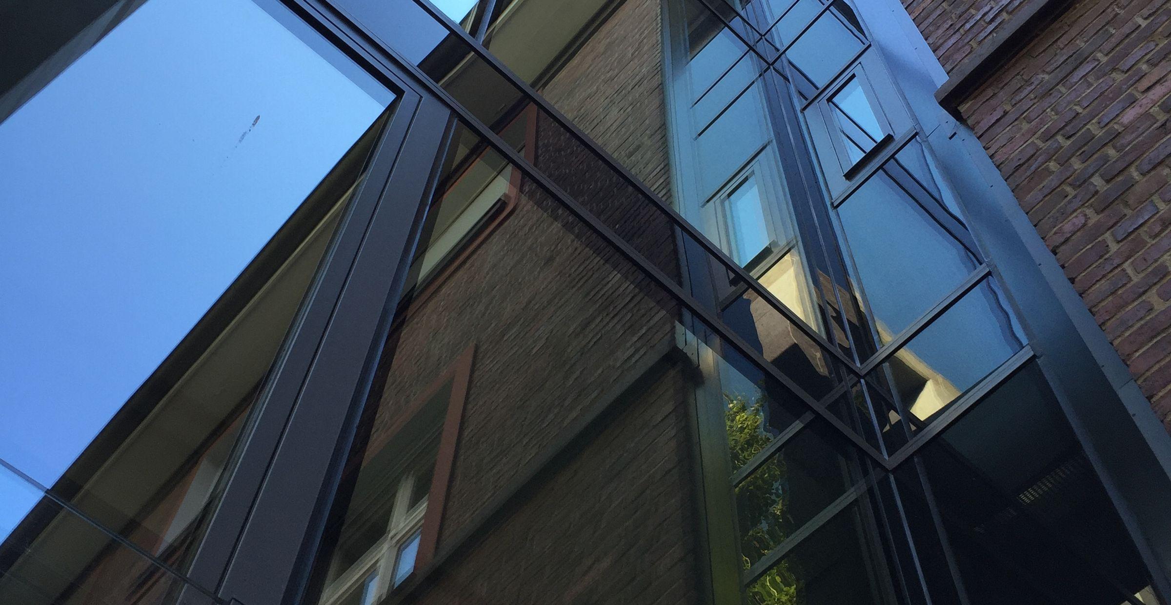 Moderne Glasfassade mit spiegelnden Elementen und Stahlprofilen.