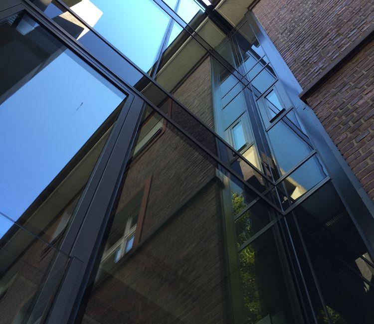 Moderne Glasfassade mit spiegelnden Elementen und Stahlprofilen.