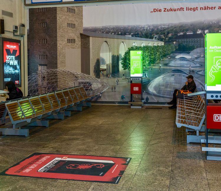 Drei DB-Ladesäulen mit Sitzbänken im Bahnhof, Werbespruch: „Auftanken mit Ökostrom!“