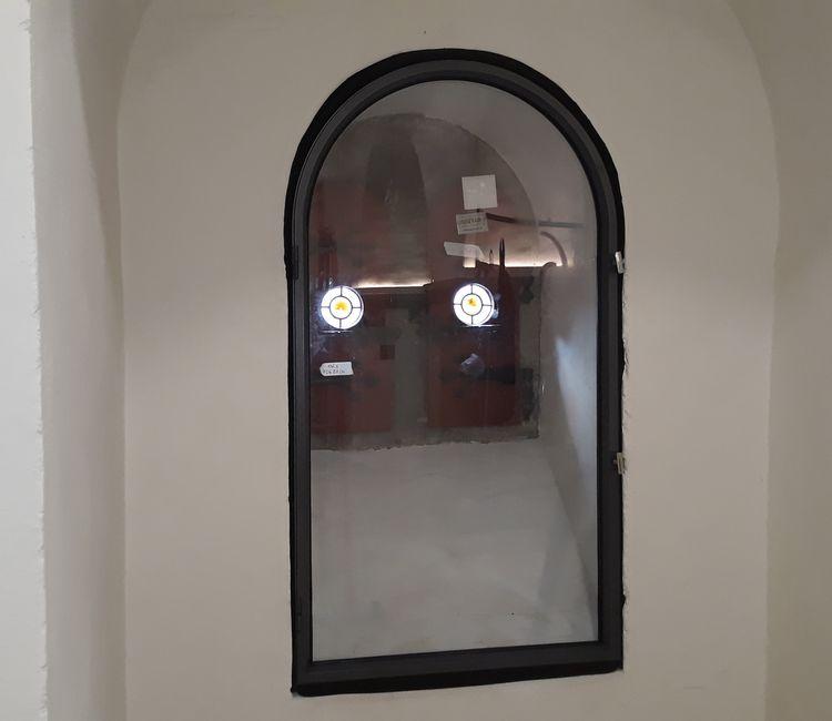 Innenansicht eines hohen Rundbogenfensters mit Blick auf ein rundes, bunt verglastes Außenfenster.
