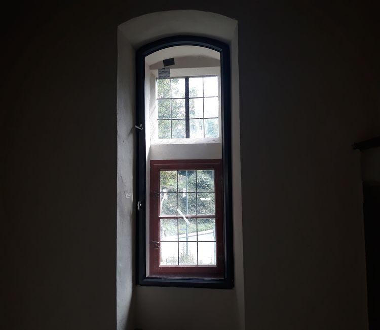 Fensteröffnung mit neu eingesetztem Isolierglasrahmen vor einem original erhaltenen Holzsprossenfenster.