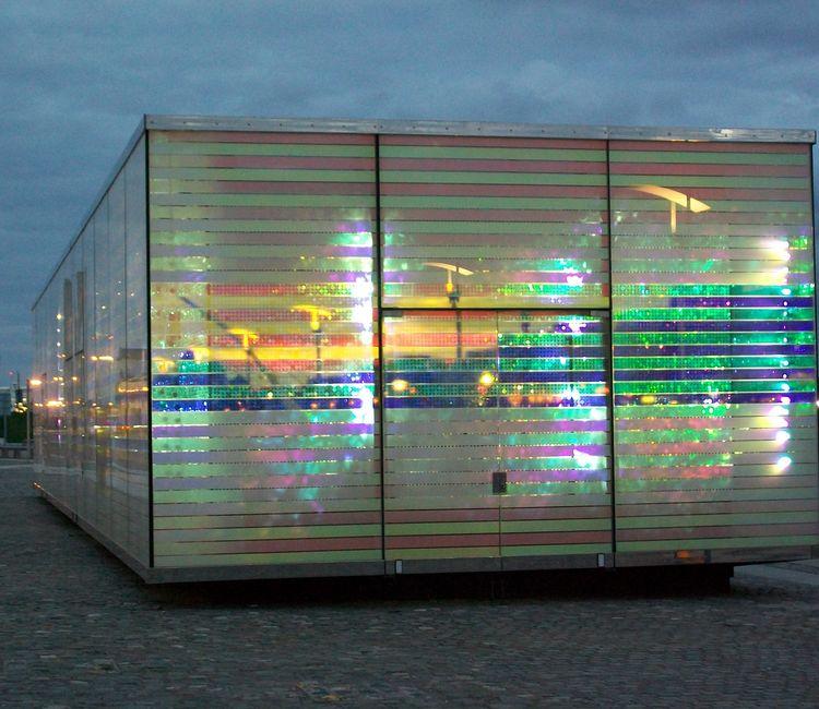 Gebäudefront bei Dämmerung mit stark reflektierenden, farbigen Glaselementen.