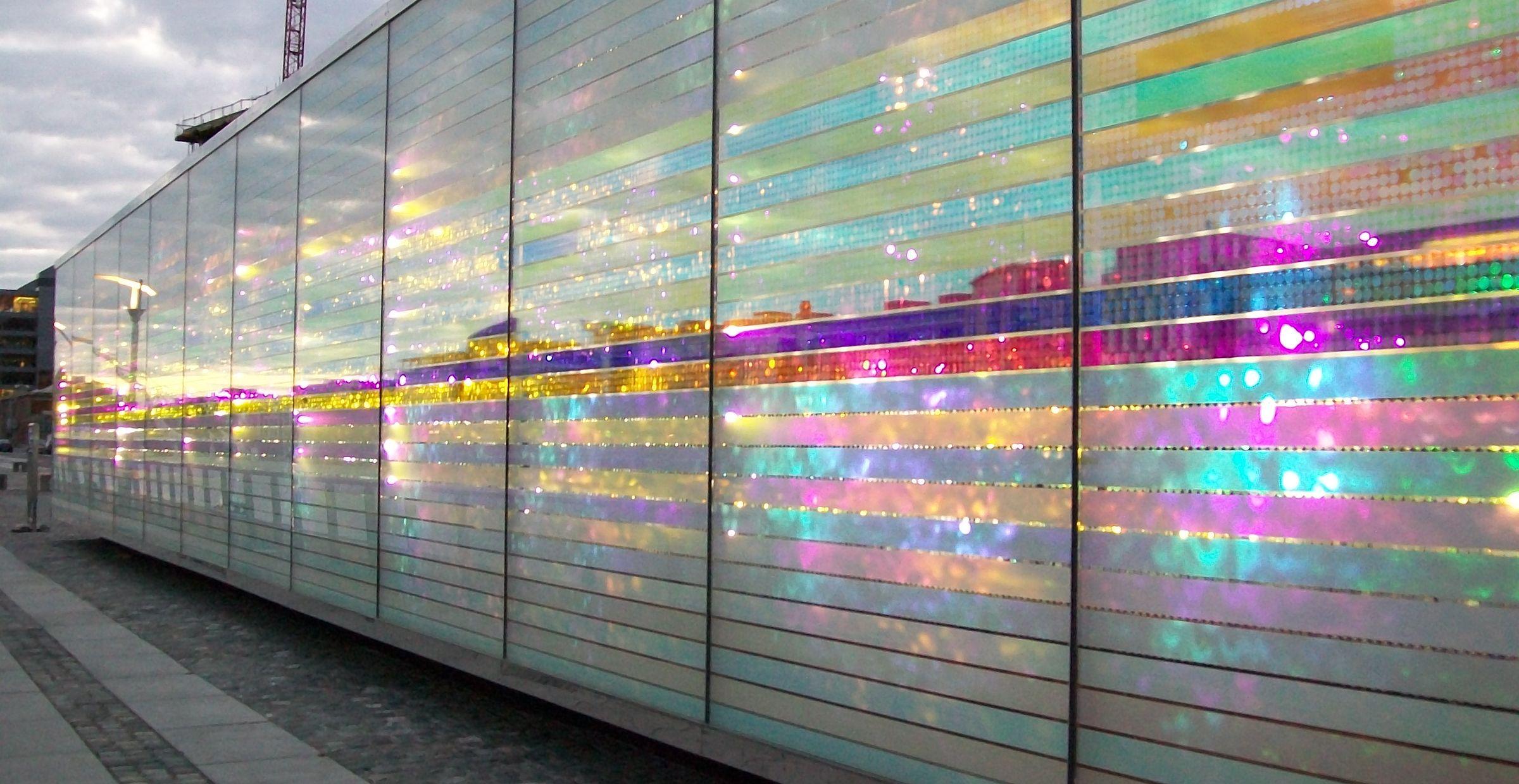 Glasfassade im Abendlicht mit leuchtenden Farben und spiegelnden Effekten.