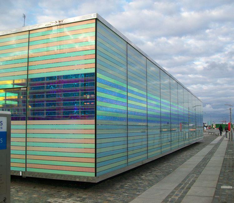 Seitliche Perspektive des Gebäudes mit schimmernden Glaselementen in bunten Farbtönen.