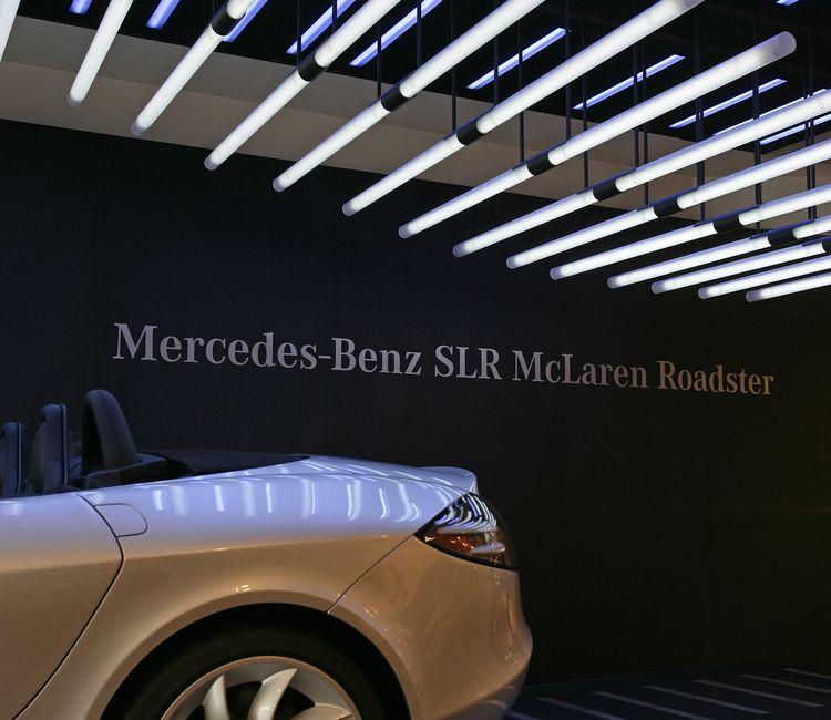 Rückansicht eines silbernen Mercedes-Benz SLR McLaren Roadster unter einer futuristischen Deckenbeleuchtung mit leuchtenden Lichtstäben.