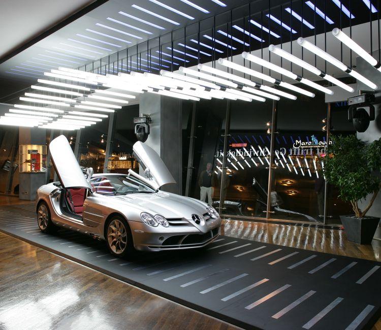 Silberner Mercedes SLR mit geöffneten Flügeltüren im stilvoll beleuchteten Mercedes-Benz Showroom.