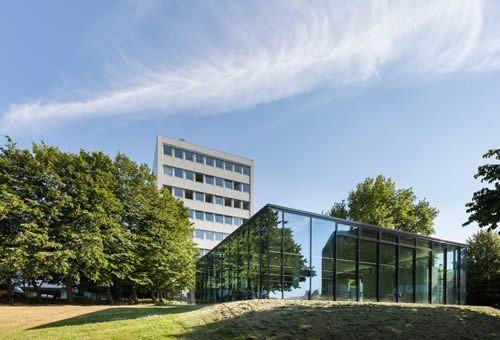 Gesamtansicht des Pavillons im Grünen mit Universitätsgebäude im Hintergrund.