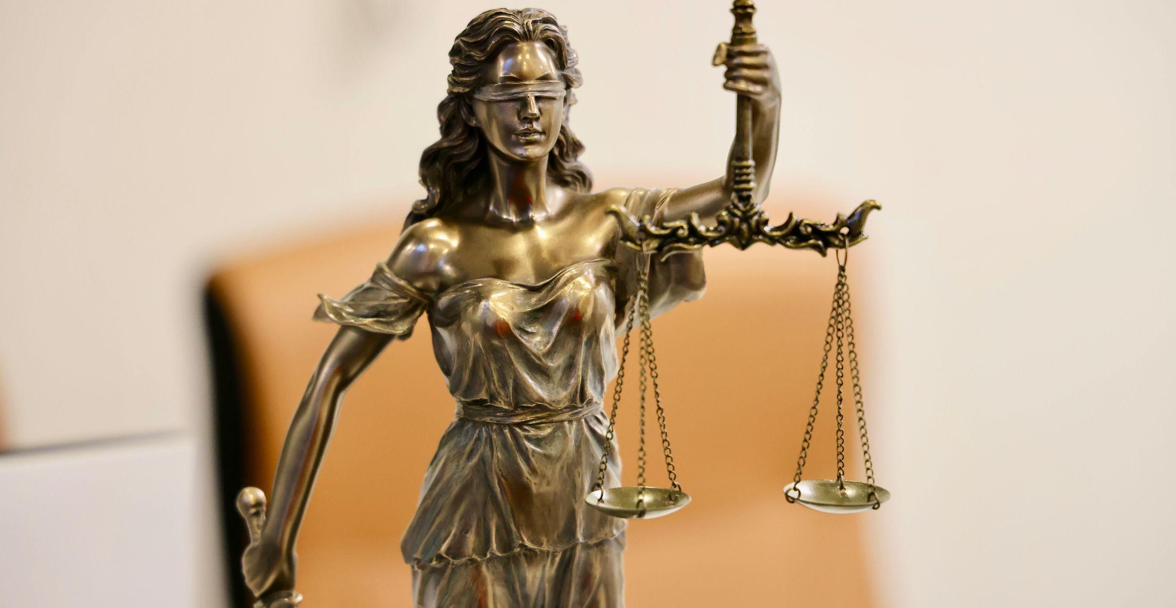 Bronzene Justitia-Figur mit verbundenen Augen und Waage in der Hand, Symbol für Gerechtigkeit.
