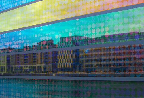 Fassade mit transparenten Farbstreifen und Sicht auf dahinterliegende Gebäude.